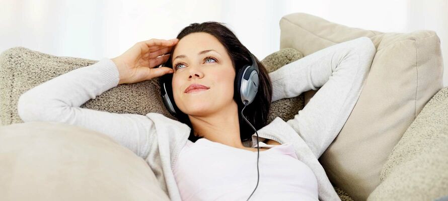 Frau liegt gemütlich auf einer Couch von ombra und hört Musik