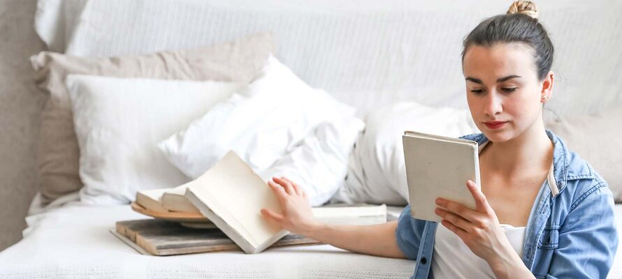 Vor Sofa mit Pölstern von ombra sitzende Frau sortiert Bücher