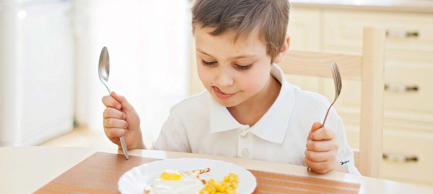 Junge freut sich auf gutes Essen, das vor ihm auf einem Tisch von ombra steht